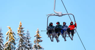 Gruppe af mennesker på en skilift med sneklædte træer i baggrunden.