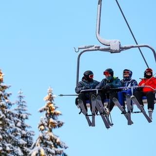 Gruppe af mennesker på en skilift med sneklædte træer i baggrunden.