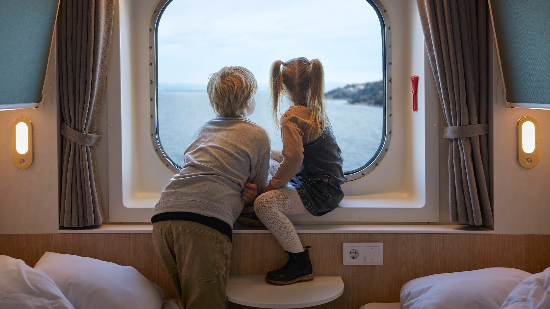 Dreng og pige sidder i vindueskarmen på en kahyt og kigger ud