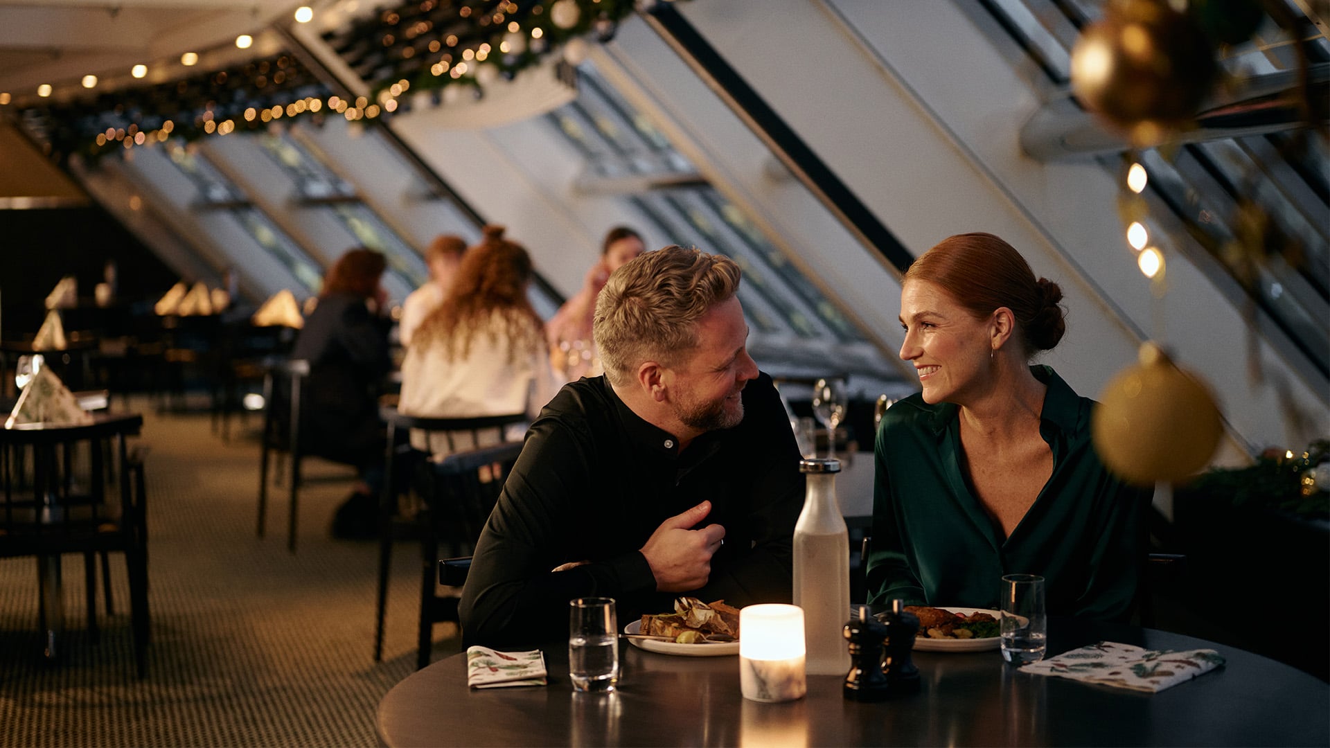 Folk der spiser på en restaurant med naturligt lys og dekorationer.