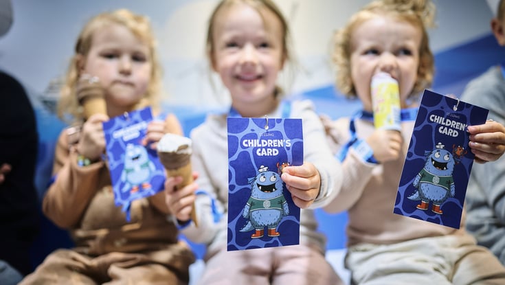 Tre børn, der holder "Children's Card"-hæfter med en tegneseriefigur i Matrosklubben.
