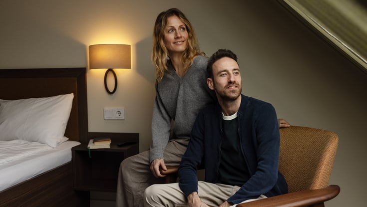 To personer i et rum med en seng og et natbord.