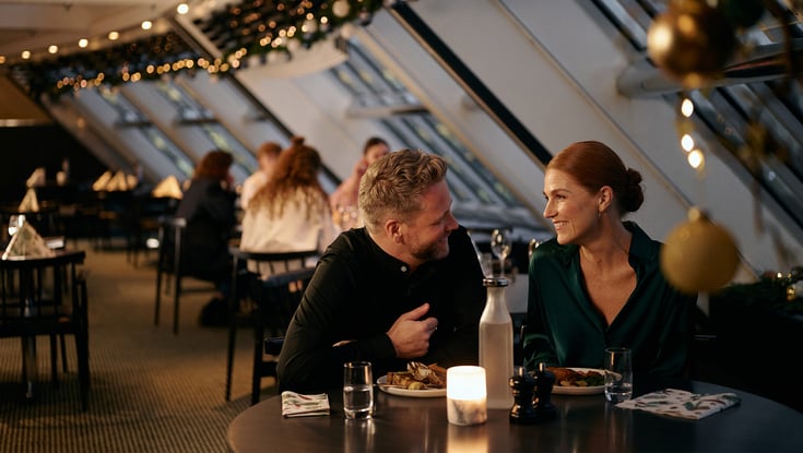 Folk der spiser på en restaurant med naturligt lys og dekorationer.