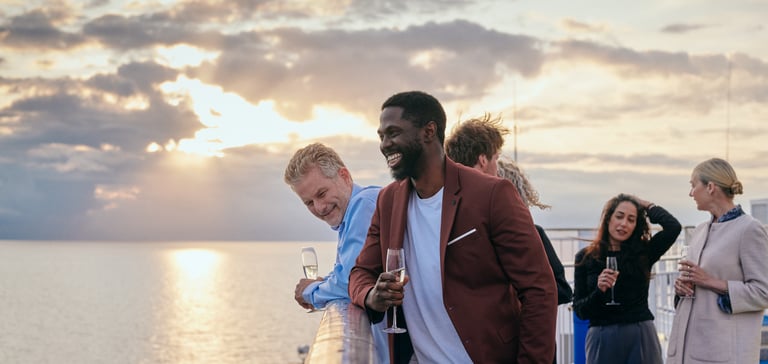 Gruppe af personer på en båd, der nyder havudsigten ved solnedgang med drikke i hånden