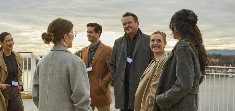 En gruppe mennesker i overtøj snakker sammen på dæk under en konference