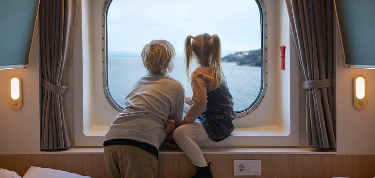 Dreng og pige sidder i vindueskarmen på en kahyt og kigger ud