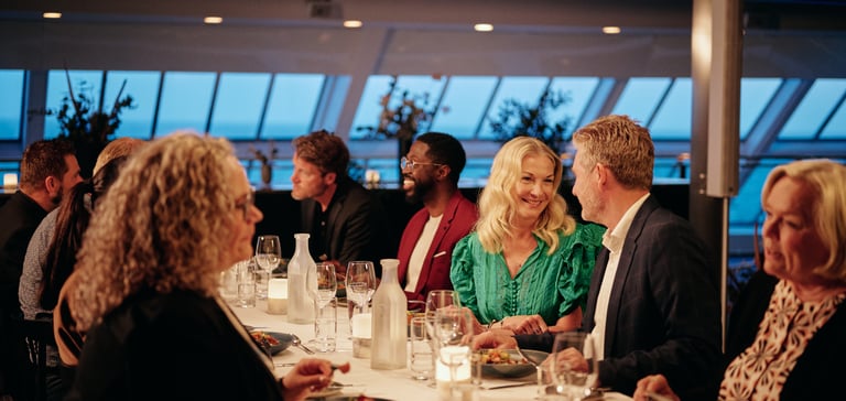Middagsselskab ved solnedgang i lyst lokale med store vinduer, stearinlys og vinglas