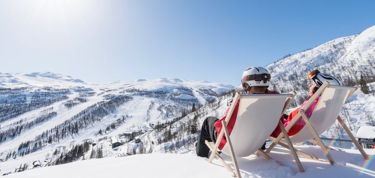 To personer sidder i liggestole på en sneklædt bakke i Hemsedal.
