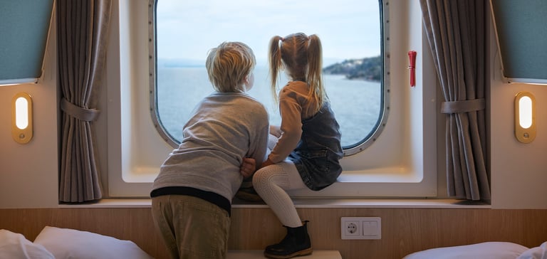 Dreng og pige sidder i vindueskarmen på en kahyt og kigger ud