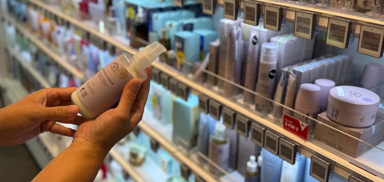 Person holder en hudplejeflaske i en butiksgang fyldt med skønhedsprodukter