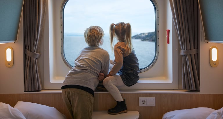 Dreng og pige sidder i vindueskarmen på en kahyt og kigger ud