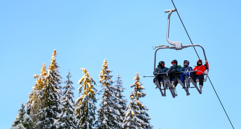 Gruppe af mennesker på en skilift med sneklædte træer i baggrunden.