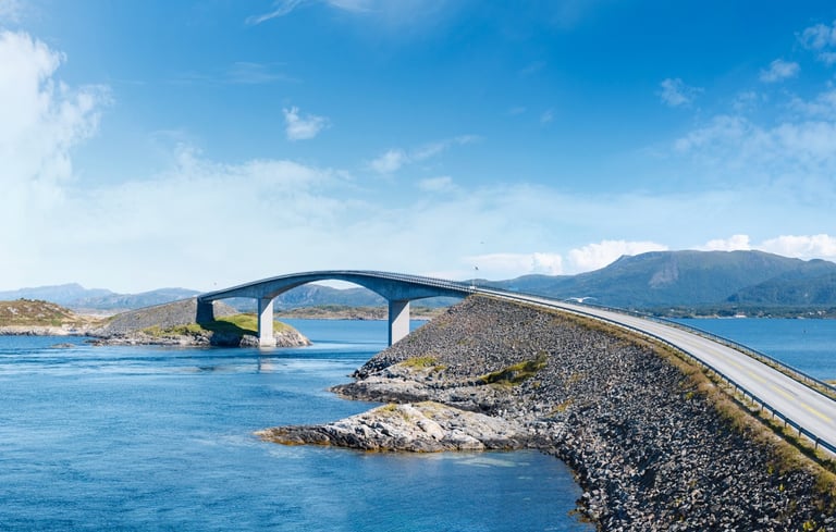 Atlanterhavsvejen - med bro over vand med bjerge i baggrunden.