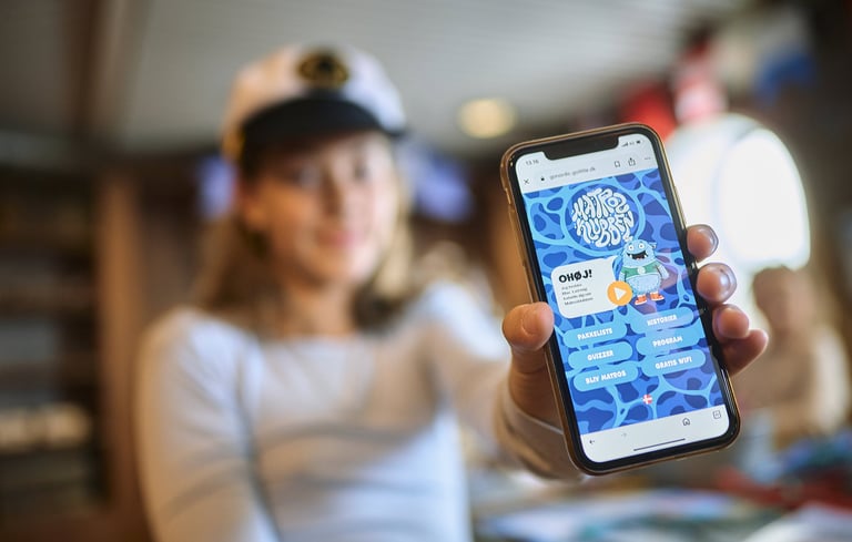 Person, der holder en smartphone, som viser en applikation eller hjemmeside relateret til Matrosklubben.