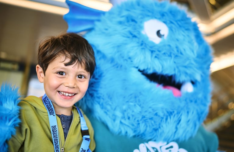 Person står ved siden af en stor blå lodden maskot med hvide øjne og et stort smil i Matrosklubben.