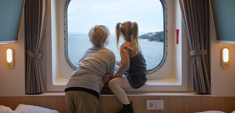 Dreng og pige sidder i vindueskarmen på en kahyt og kigger ud