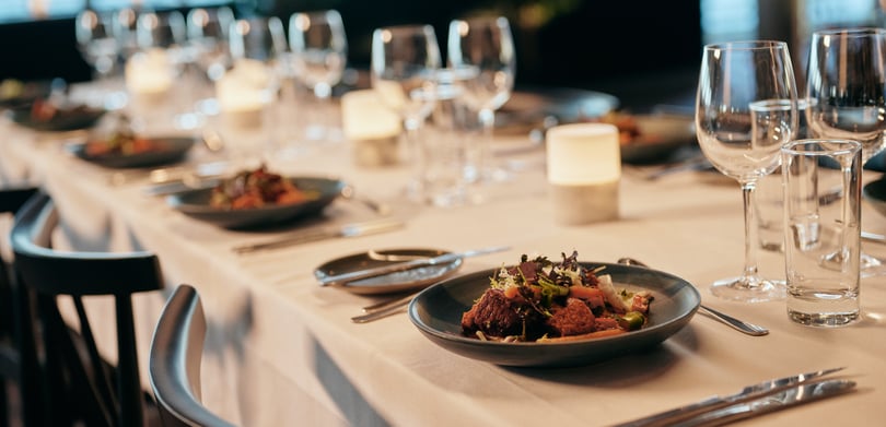 Elegant dækket spisebord med hvid dug, salater, bestik, stearinlys og vinglas
