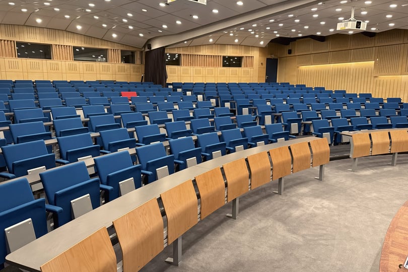 Tomt auditorium med blå sæder og træborde
